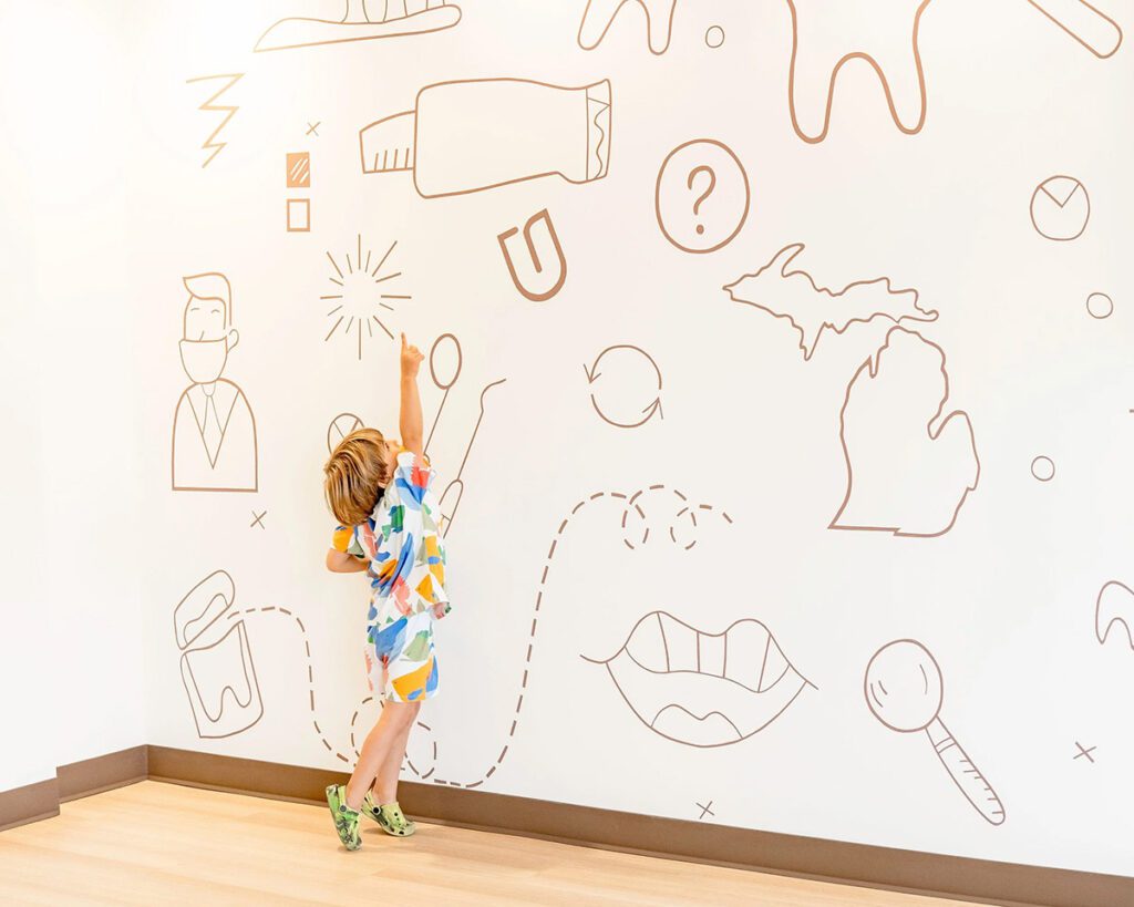 Child pointing at dental-themed wall illustration in pediatric dental office