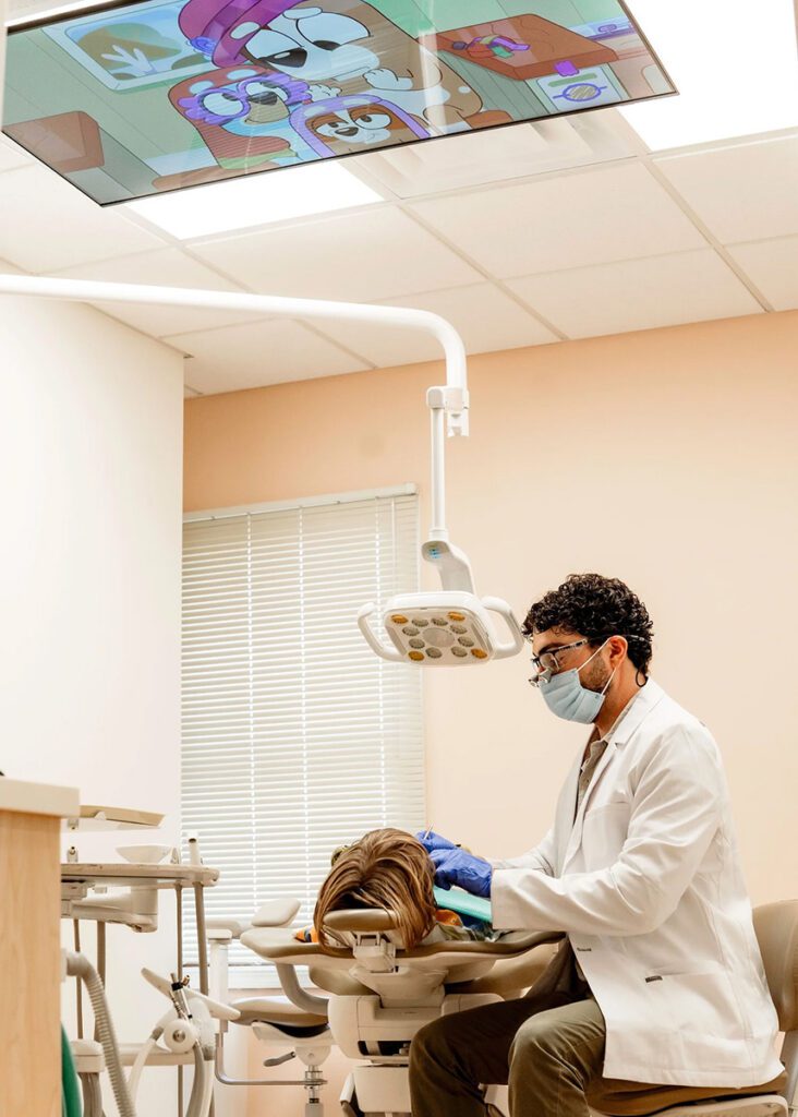 Pediatric dentist performing dental treatment on child in exam room